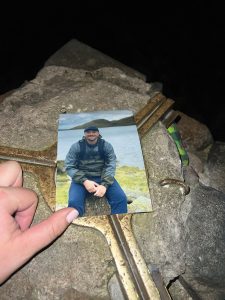 A hand leaving a photograph of Gaz Emmerson on top of one of the Three Peaks. 