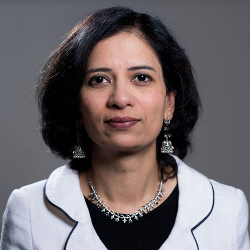 Professional portrait of Dr Priya Suresh, a radiologist with shoulder-length dark hair, wearing a white blazer over a black top with an ornate silver necklace.