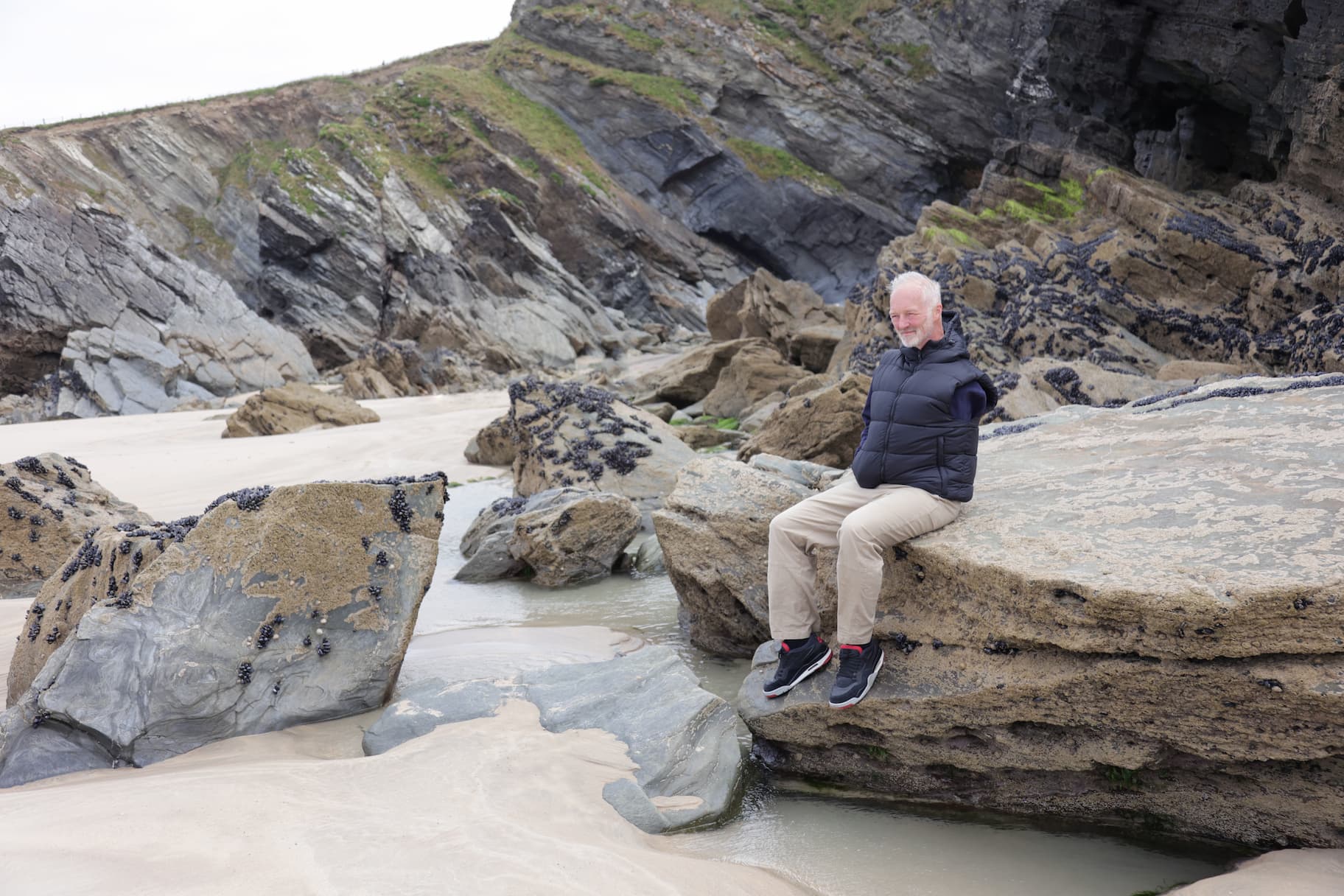 Photo on man sitting on rocks on a beach.