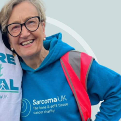 Photo of woman wearing glasses and a Sarcoma UK branded top looking at camera.