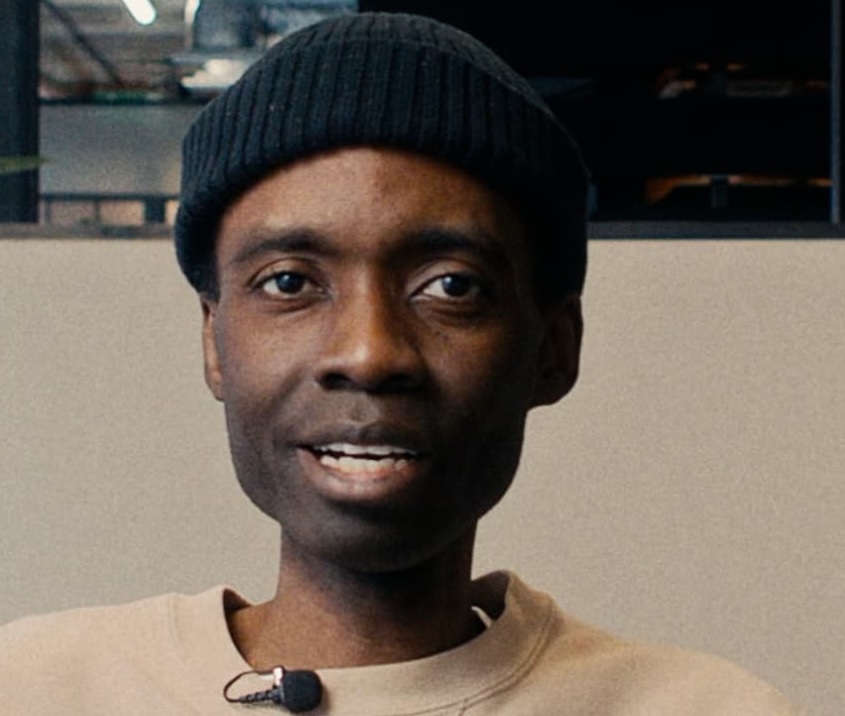 Photo of Roy Mugera, looking directly at camera. He is wearing a black hat.