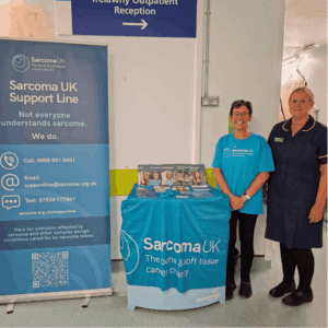 Helen from the Sarcoma UK Support Line with a nurse at an information stand in a hospital outpatient area.